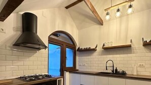 Ett modernt kök med vita skåp, en svart spis, ett träpanelat tak och ett fönster.