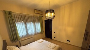 Ein Hotelzimmer mit einem Bett, einer Chandelüster, einem Vorhangfenster, einer Tür und einer Klimaanlage.