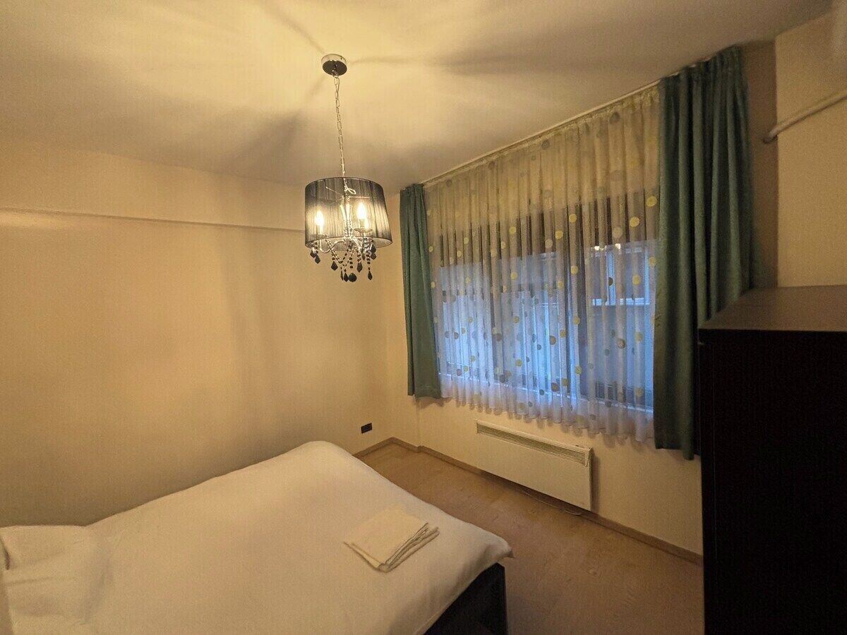 En enkeltseng med et hvidt lagen, en loftsvifte, et vindue med lette gardiner og en radiator.