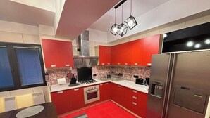 Eine moderne Küche mit roten Schränken, einem Edelstahl-Kühlschrank, einem Einbauofen und einem Gasherd.