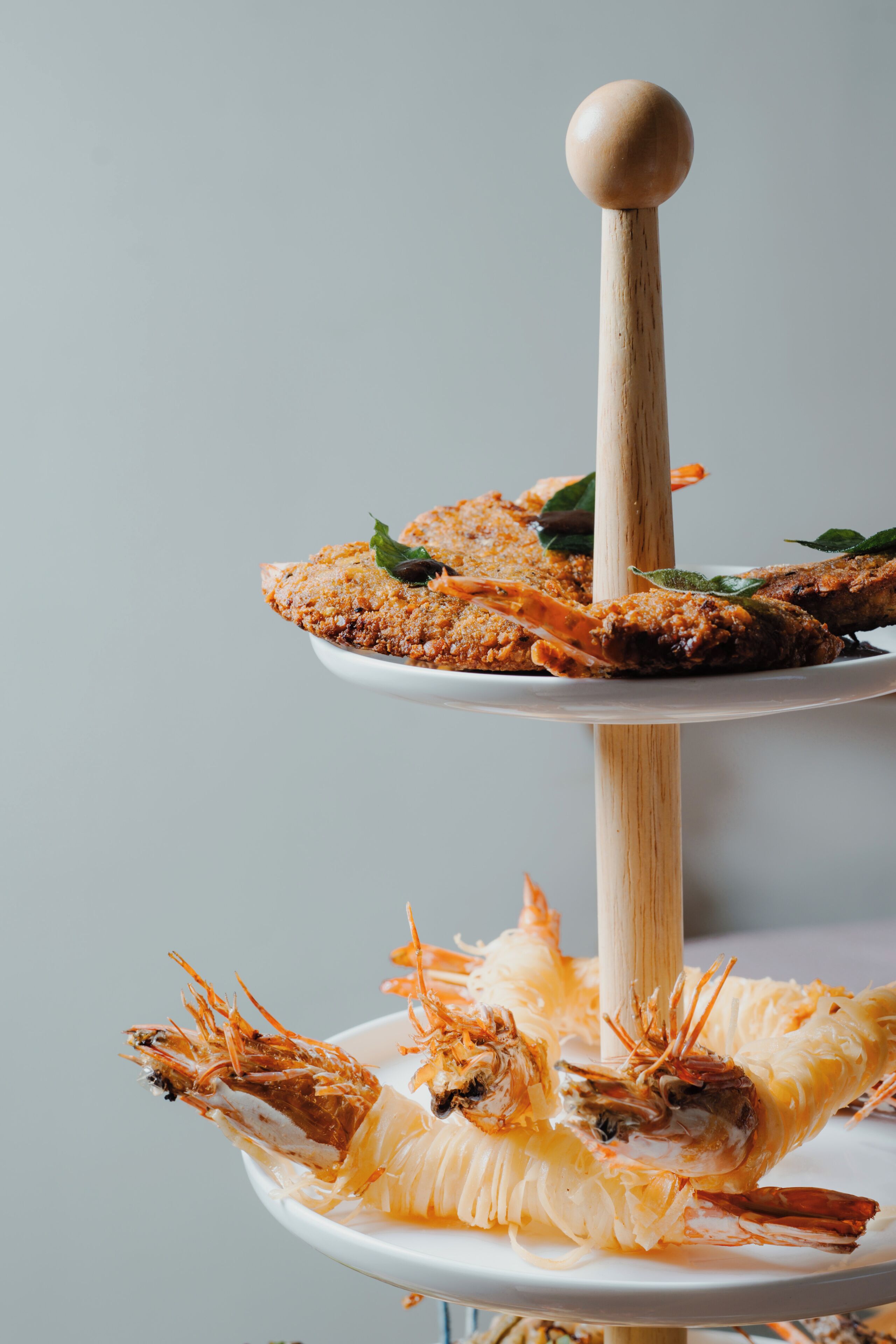 Un plato de varios niveles con mariscos, un asa de madera y un fondo liso.