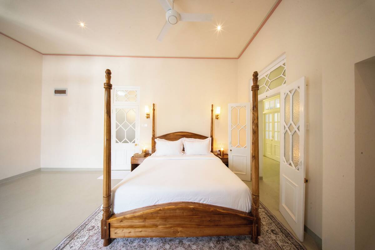A four-poster bed with a wooden frame, a ceiling fan, and wall-mounted lights.