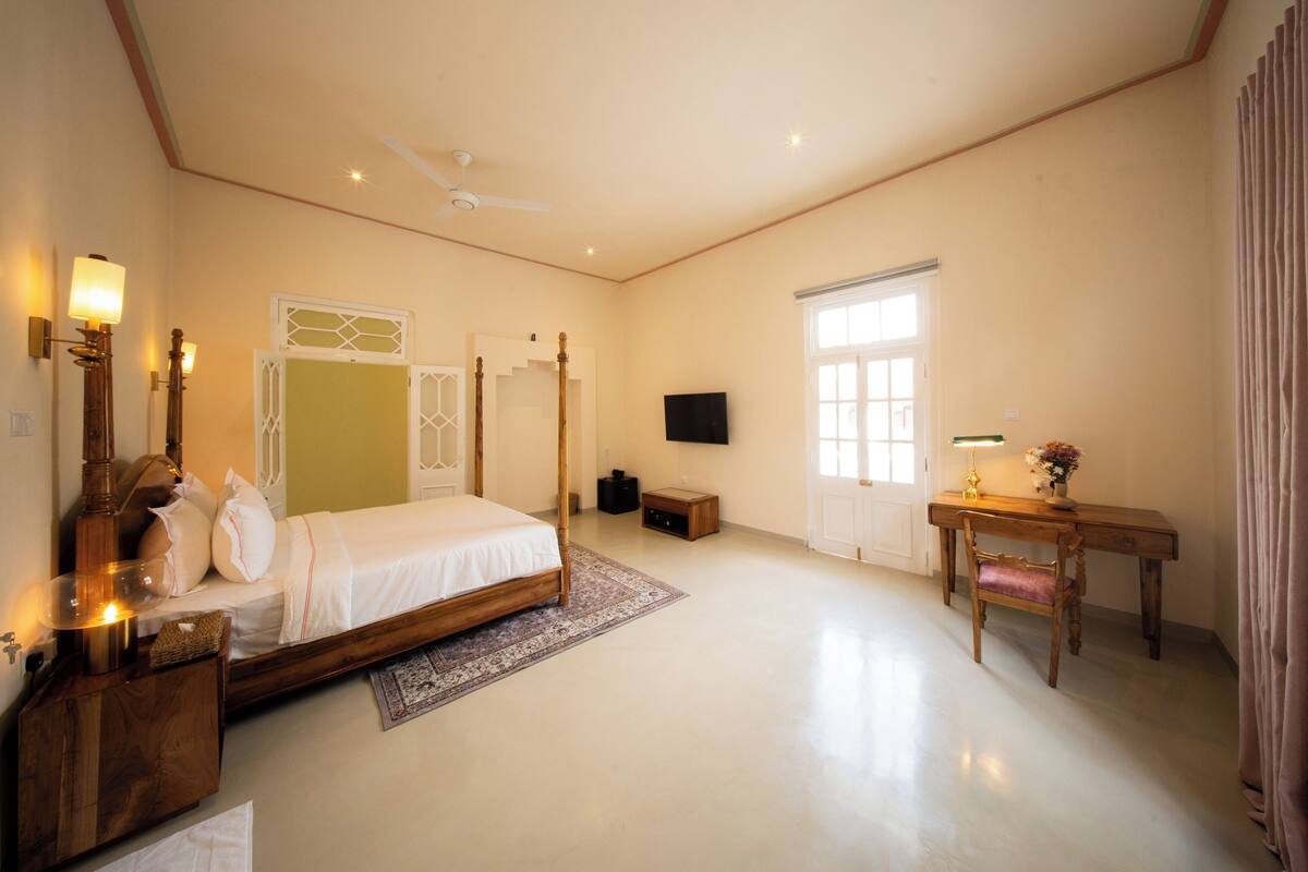 A bedroom with a bed, bedside table, lamp, and a desk with a chair.