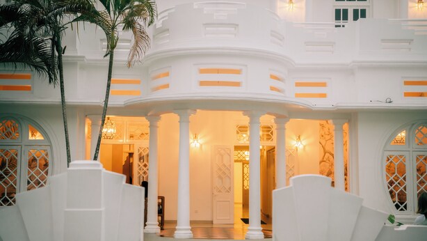 A white building with a circular central courtyard, columns, and a palm tree. - Padmaraga (Galle)