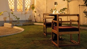 A room with a wooden chair, a table, and a lamp. There is a window with a view of a building outside. - Padmaraga (Galle)