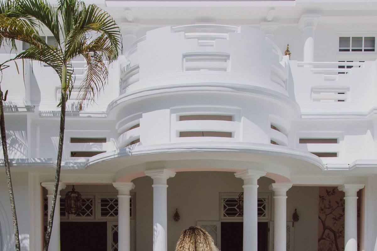 A woman in a floral dress walking towards a white building with columns and a covered entrance.