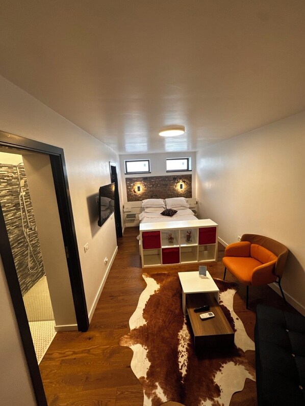 Ein kompaktes Hotelzimmer mit Bett, einer kleinen Sitzecke, einem Kuhfellteppich und einem an der Wand befestigten Fernseher.