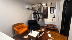 A compact living space with a sofa, a chair, a small table, a cowhide rug, a bench, and a partition with vertical bars. - Cismigiu Ground Floor w Garden View Apartment (Bucharest)