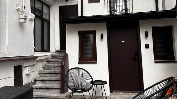 A two-story building with a brown door, a staircase leading to the upper floor, and two black chairs in the courtyard. - Cismigiu Ground Floor w Garden View Apartment (Bucharest)