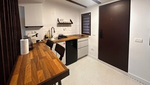 A compact kitchen with a wooden dining table, a built-in dishwasher, and a small countertop. - Cismigiu Ground Floor w Garden View Apartment (Bucharest)