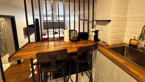 A modern kitchen with a wooden countertop, bar stools, a sink, and a view of the living area through a partition. - Cismigiu Ground Floor w Garden View Apartment (Bucharest)