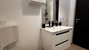 Un baño moderno con inodoro, lavamanos, espejo y ducha.