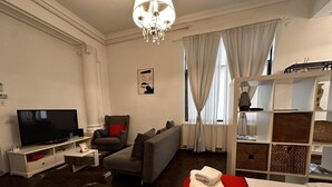 Una sala de estar con televisor, sofá, sillón y una cama roja.