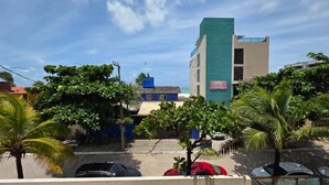 A street view with buildings, parked cars, and palm trees. - Porto Baobas Vista Mar 102 By LP (Ipojuca)