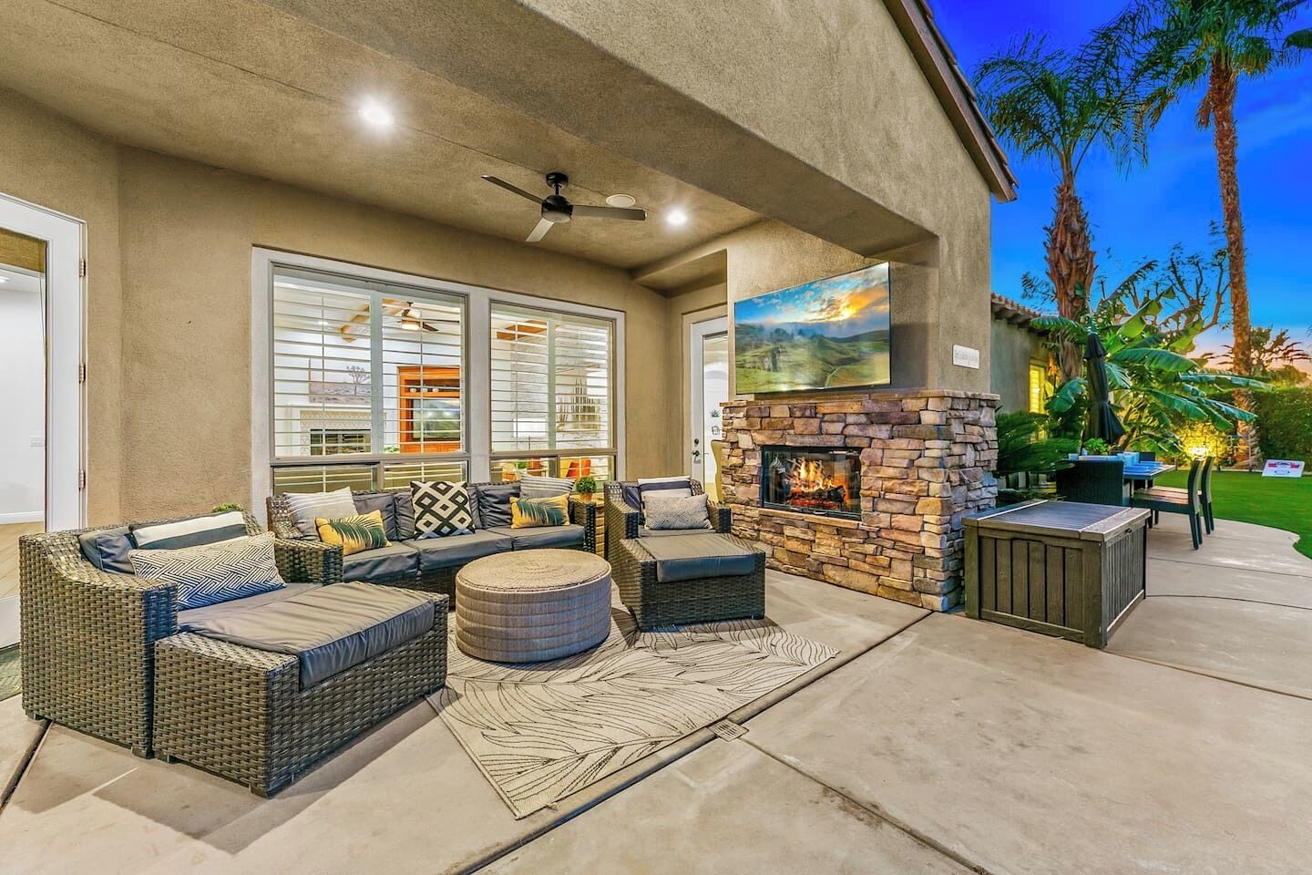 An outdoor patio with wicker furniture, a stone fireplace, and a view of the garden.