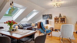 Una stanza in stile loft con zona pranzo, divano, poltrona blu, mobile contenitore e finestra a lucernario.
