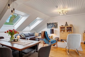 Ein Loft-Zimmer mit Essbereich, einer Couch, einem blauen Sessel, einem Schrank und einem Dachfenster.