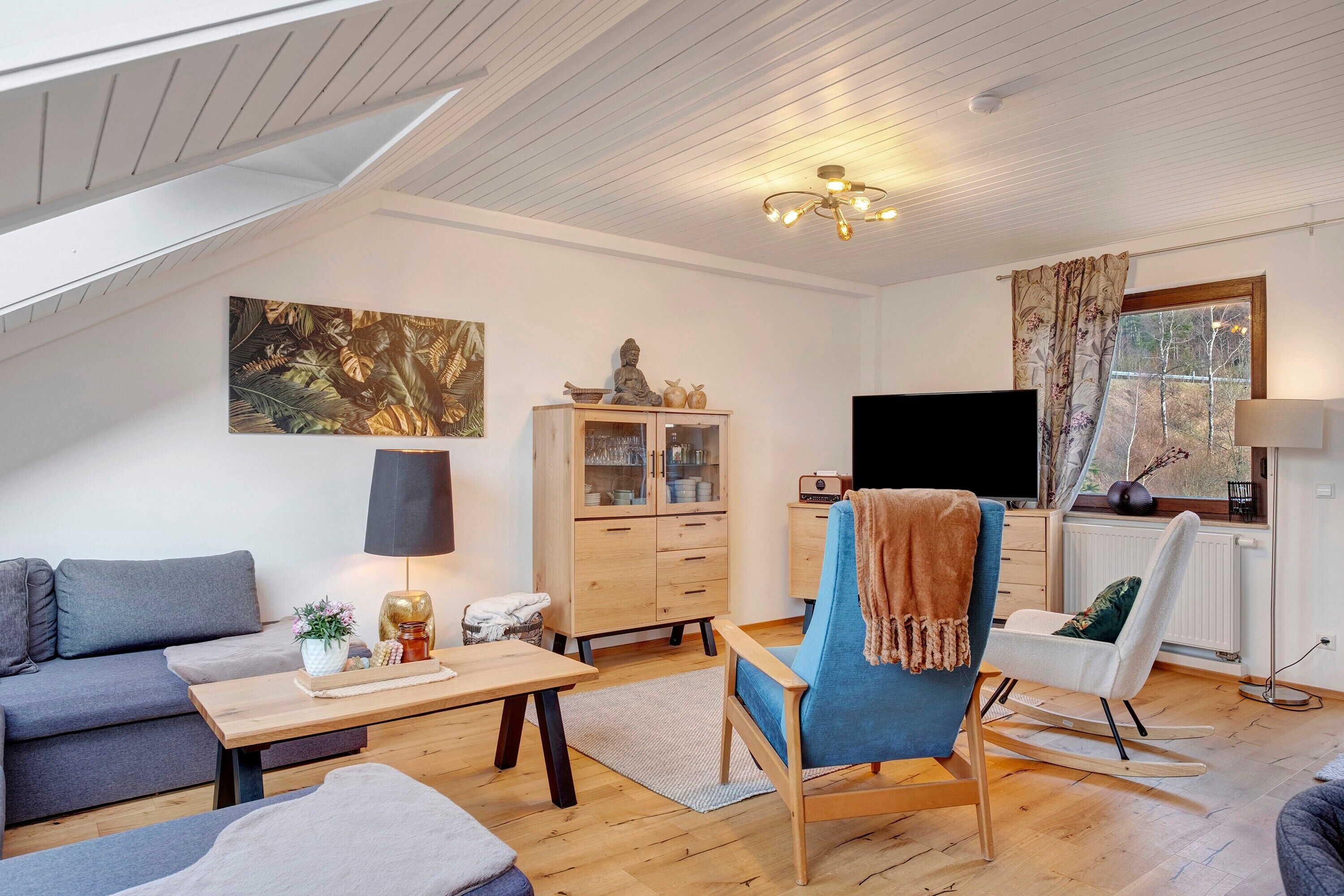 A modern living room with a sofa, a rocking chair, a coffee table, a cabinet, a TV, and a window with curtains.