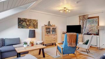 A modern living room with a sofa, a rocking chair, a coffee table, a cabinet, a TV, and a window with curtains.