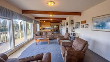 A spacious living area with a large window, a kitchen in the background, and a dining area.