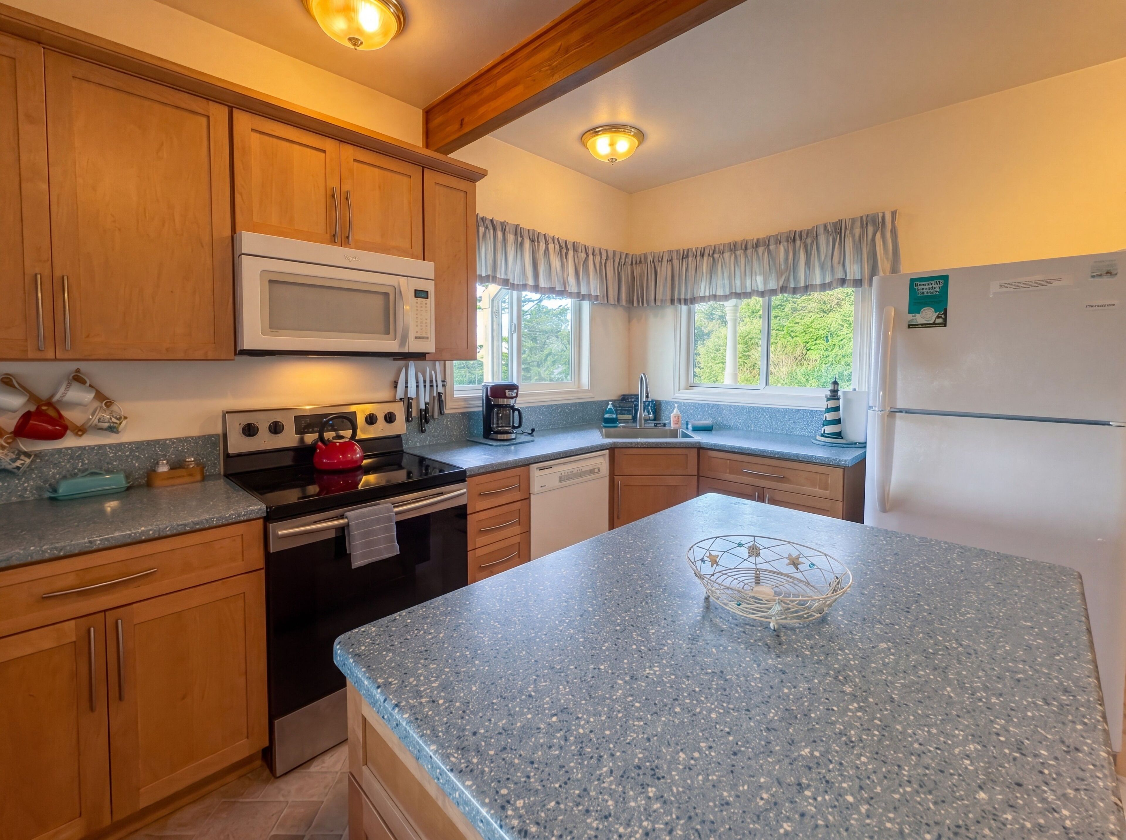 A kitchen with wooden cabinets, a microwave, a kettle, and a refrigerator.