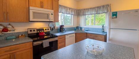 A kitchen with wooden cabinets, a microwave, a kettle, and a refrigerator.