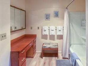 Een badkamer met een houten wastafelmeubel, een bankje, een bad en een douchegordijn.