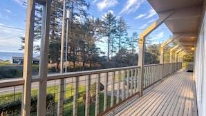 Eine Holzterrasse mit Geländer, mit Blick auf eine Straße und Grünflächen.