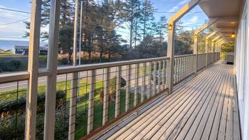 A wooden deck with a railing, overlooking a road and greenery.