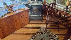 Una cabaña acogedora con un interior rústico, suelo de madera, estufa, sillón y vistas a un lago.