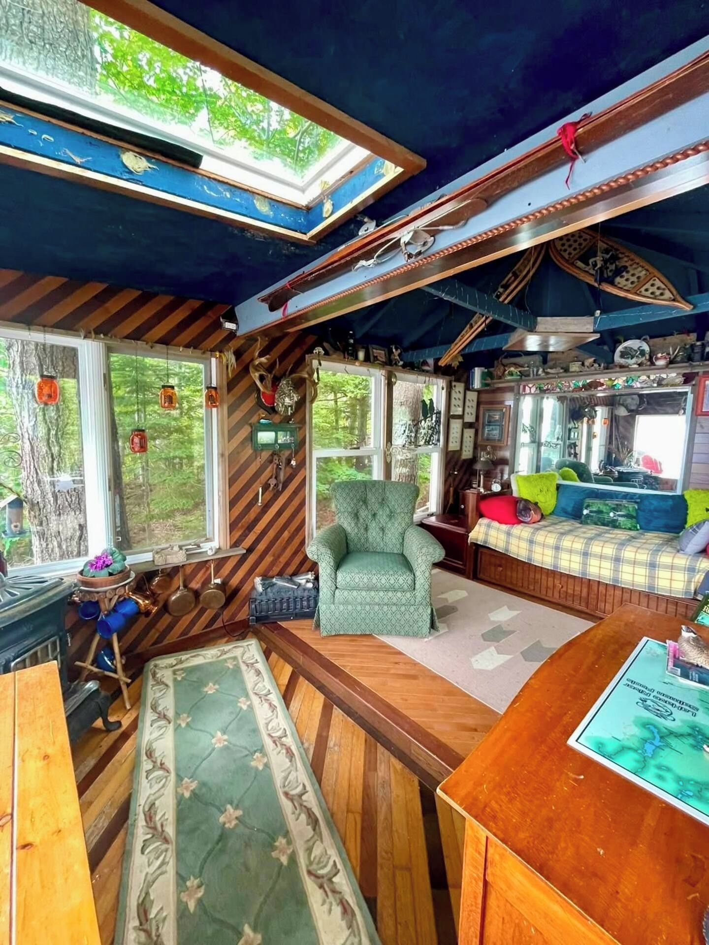 Ein gemütliches Blockhausschlafzimmer mit großem Fenster, einem grünen Sessel, einem karierten Sofa und Holzboden.