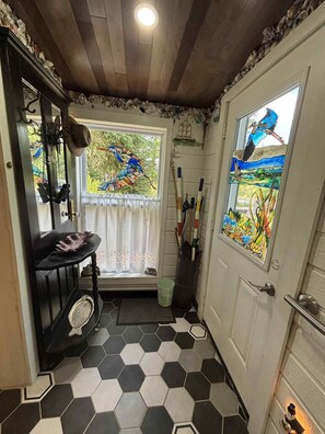 A room with a hexagonal tile floor, a door with a stained glass window, and a window with a view of greenery. - Mermaid's Retreat - Caribou Lake Cottage! (Mahone Bay)
