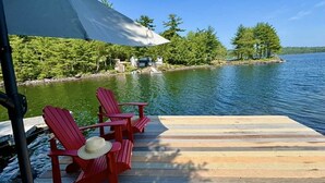 A wooden dock with red Adirondack chairs and a white umbrella.