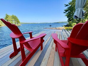 Een houten terras met rode Adirondack-stoelen gericht op een wateroppervlak.