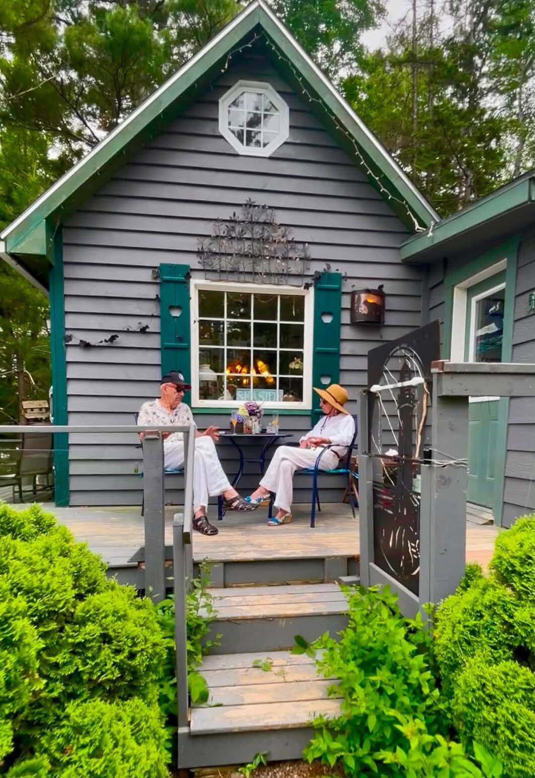 A small wooden structure with a porch, two chairs, and a table.