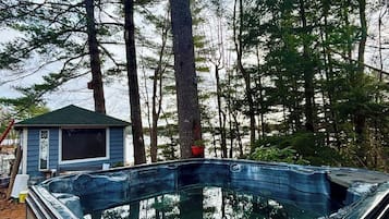 Un bain à remous entouré d’arbres, avec une maison en arrière-plan.