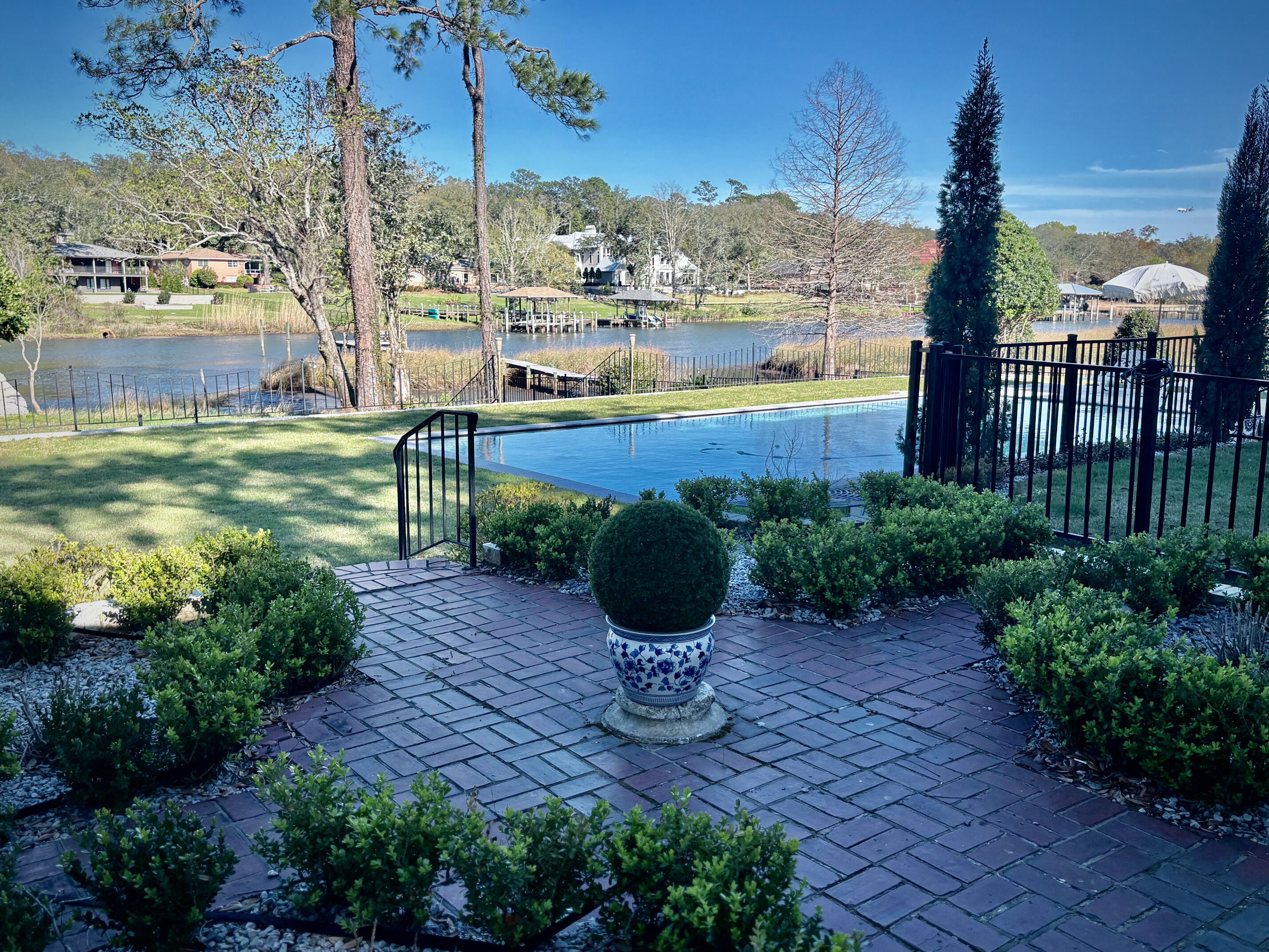 A swimming pool with a paved deck, surrounded by greenery and a fence.