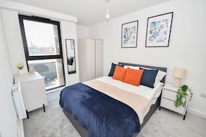 Ein modernes Schlafzimmer mit einem großen Bett, einem Kleiderschrank, einem Schreibtisch und einem Fenster mit Blick auf die Stadt.