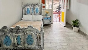 Un dormitorio con techo de madera, una cama con cabecera decorada, una planta en maceta y vistas a través de un puerta abierta.