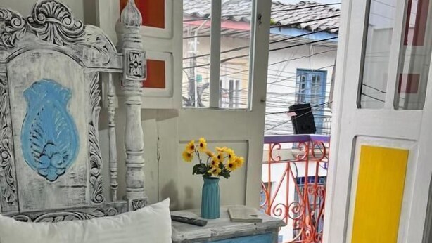 Un dormitorio con cama, cómoda, un florero con flores y vistas al exterior.