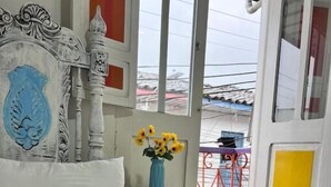 Un dormitorio con cama, mesita de noche, un jarrón con flores y un balcón con barandilla roja.
