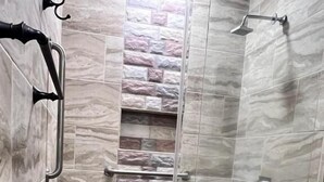 Ducha con puerta de vidrio, paredes de mármol y baranda de metal.