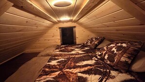 Un dormitorio acogedor en el ático con techo inclinado, una cama con colcha estampada y una lámpara circular.