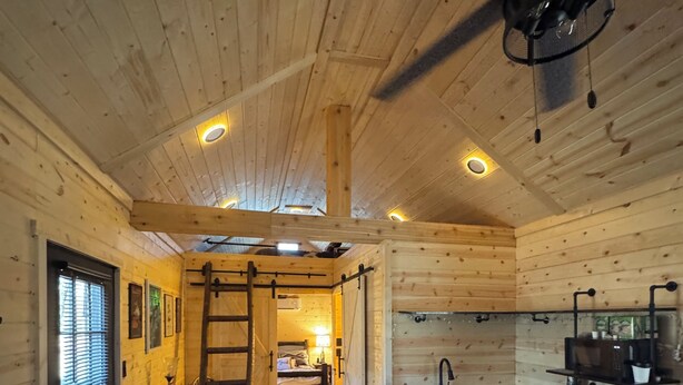 Interior acogedor de una cabaña con cama, comedor, cocina y escalera.