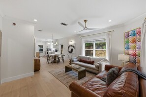 A spacious living area with a dining table, sofa, and a large window with curtains. - Zilker Home | Walk to Zilker/ACL/Barton Springs (Austin)