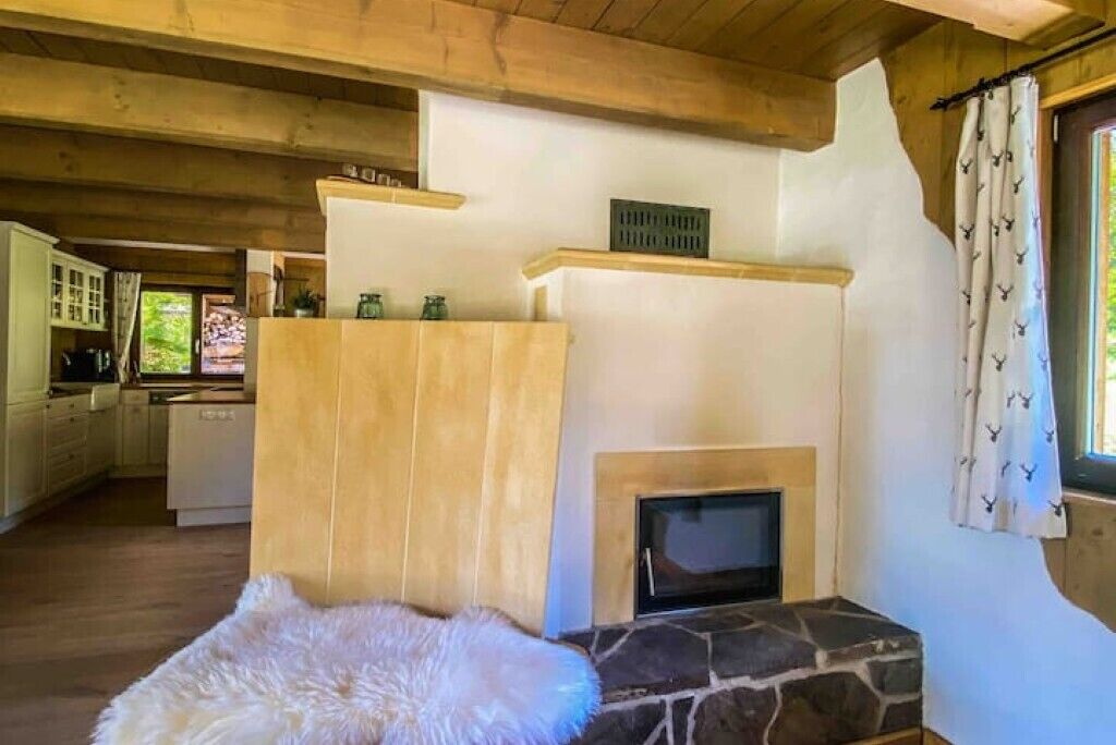 Ein rustikales Interieur mit Kamin aus Stein, Holzbalken, einem Fellteppich und einem in der Ferne erkennbaren Küchenbereich.