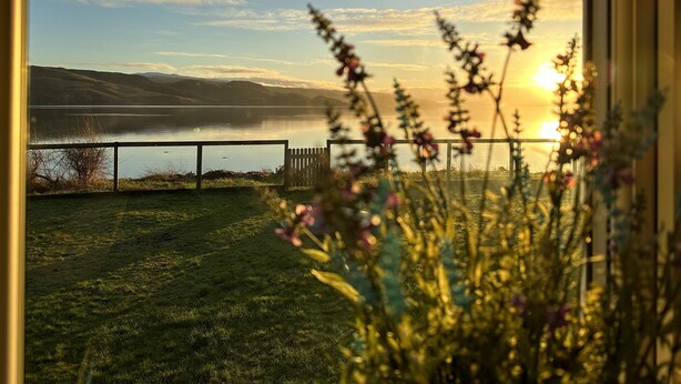 A view of a lake with mountains in the background, a fence in the foreground, and flowers in the foreground. - Super Pet-Friendly, Loch Front Cottage with Direct Loch Access and Games Room (Inveraray)