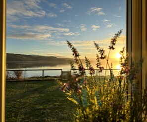 Une vue d’un lac avec des montagnes en arrière-plan, une clôture au premier plan et des fleurs au premier plan.