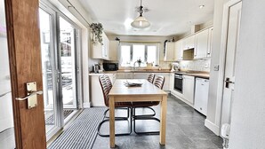 A modern kitchen with a dining table, chairs, a microwave, oven, and a hanging light fixture. - Super Pet-Friendly, Loch Front Cottage with Direct Loch Access and Games Room (Inveraray)
