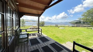 A covered patio with a view of a lake and hills, wooden benches, and a picnic table. - Super Pet-Friendly, Loch Front Cottage with Direct Loch Access and Games Room (Inveraray)